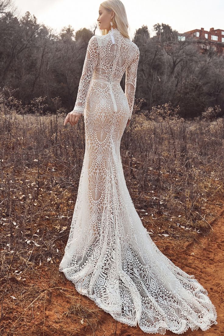 a woman in a long white dress standing on a dirt road with her back to the camera