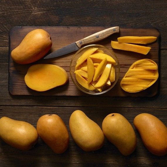 a cutting board topped with sliced up mangoes and pieces of cheese next to a knife