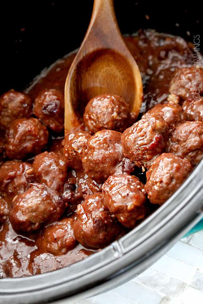 meatballs and gravy in the slow cooker being stirred with a wooden spoon