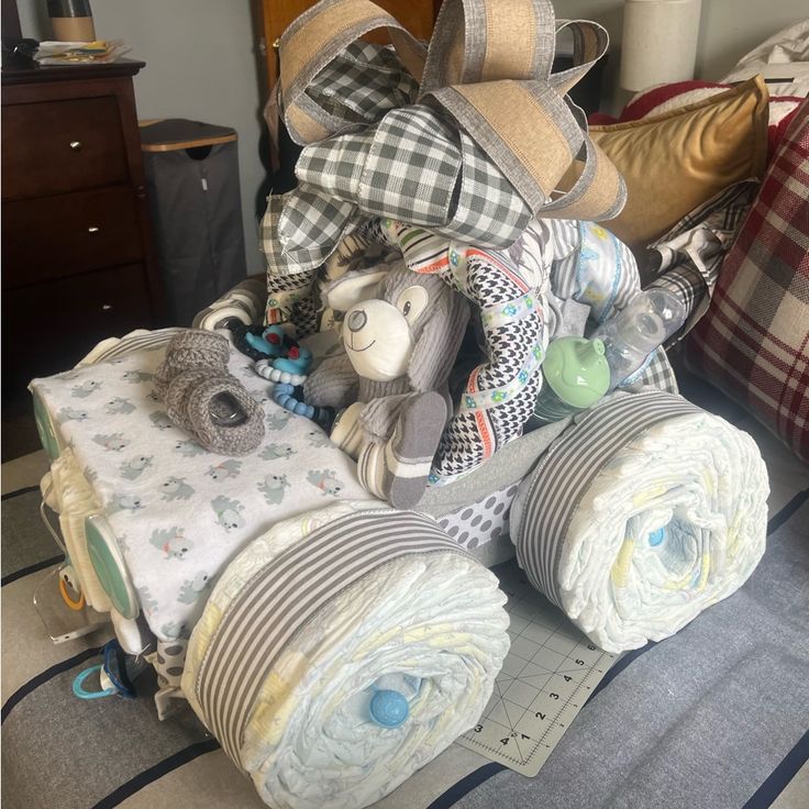 a pile of baby blankets and toys on the floor next to a bed with plaid pillows