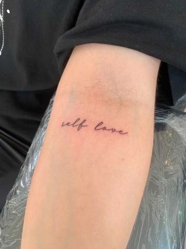 a woman with a tattoo on her arm that says self love in cursive writing