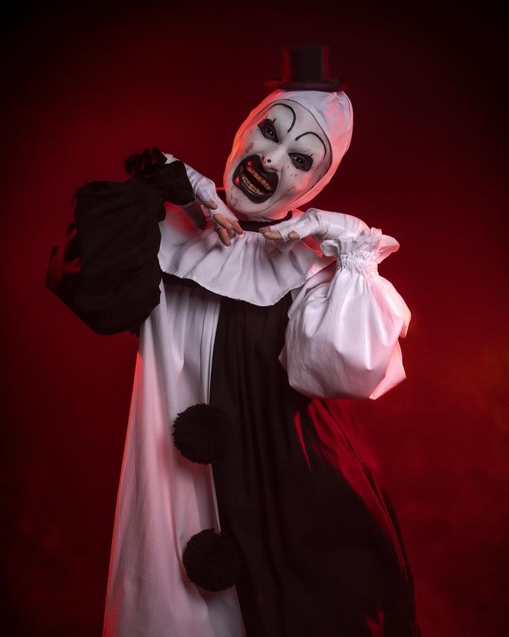 a creepy clown dressed in white and black holding a bag with his hands on his hips