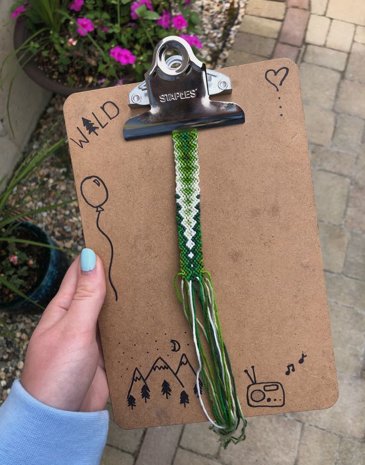 a hand holding a clipboard with some string attached to it and flowers in the background