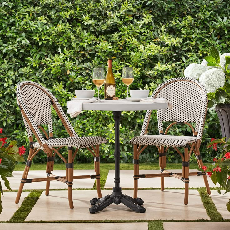 two chairs and a table in front of some bushes