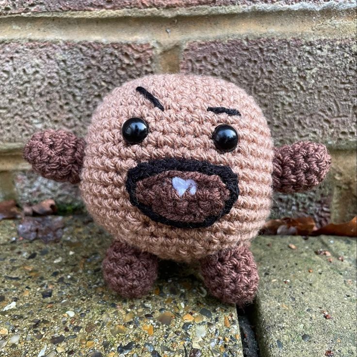 a small crocheted stuffed animal sitting on top of a cement wall next to a brick wall