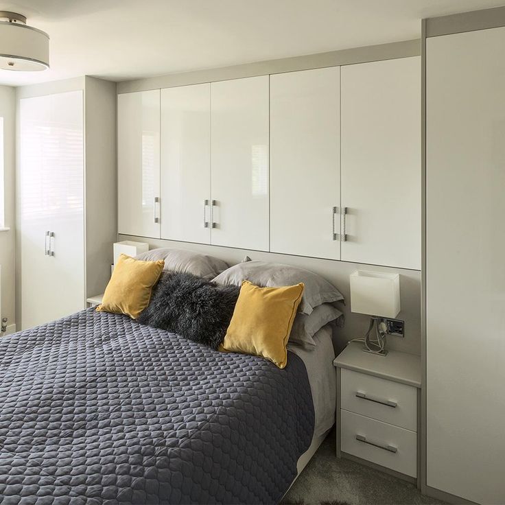 a bedroom with white cabinets and gray bedspread, yellow throw pillows on the bed