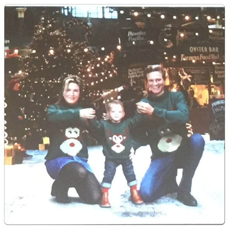 two adults and a child posing in front of a christmas tree