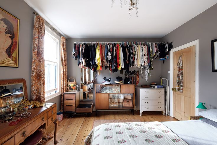 a bedroom with a bed, dresser and clothes hanging on the rack in front of it