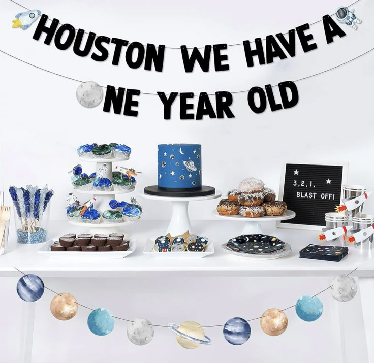 a table topped with cakes and cupcakes next to a banner that says houston we have a new year old