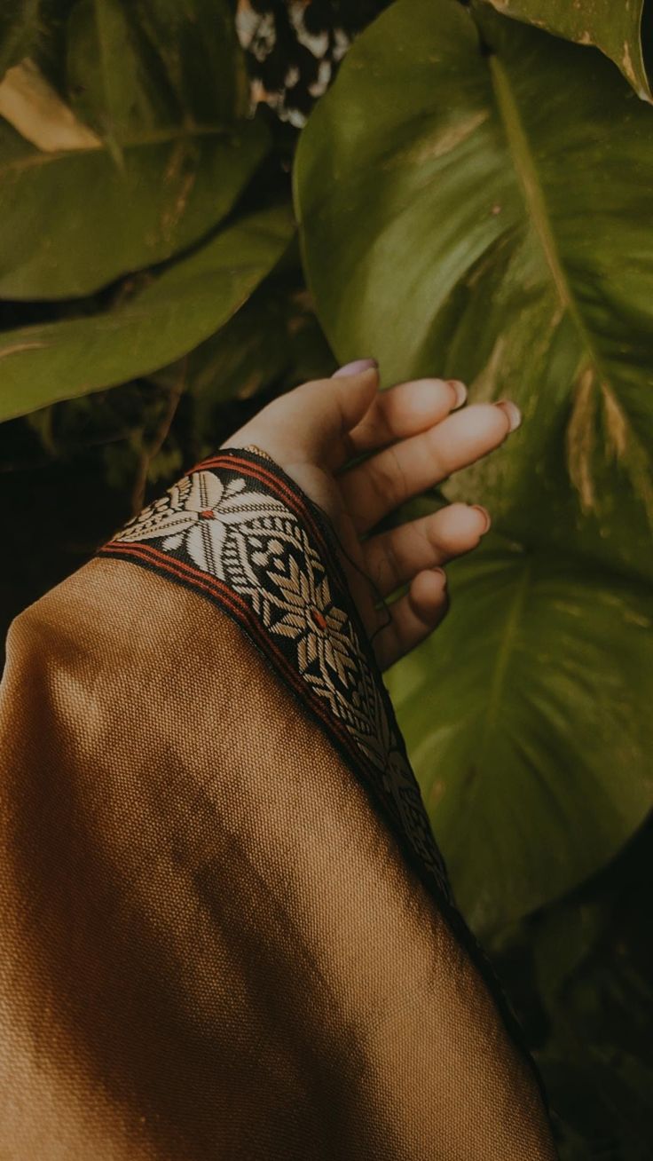 a woman's hand with a bracelet on her wrist next to some leaves and plants