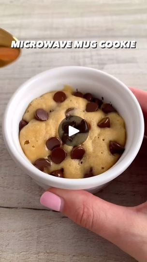 a hand holding a white bowl filled with chocolate chip cookie