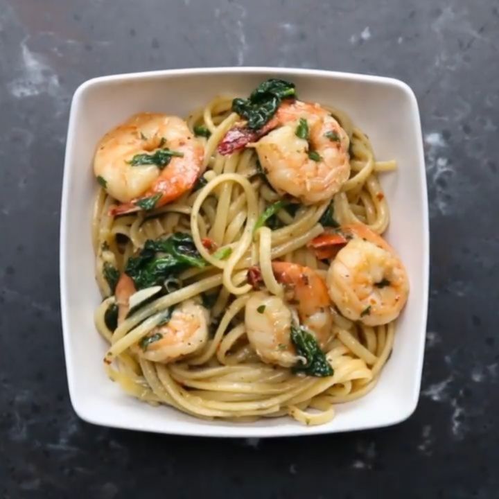 pasta with shrimp, spinach and sun dried tomatoes in a white bowl on a black table