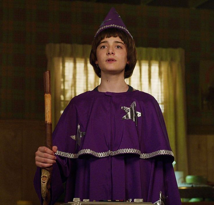 a young man dressed in purple holding a wooden stick and wearing a priest's outfit