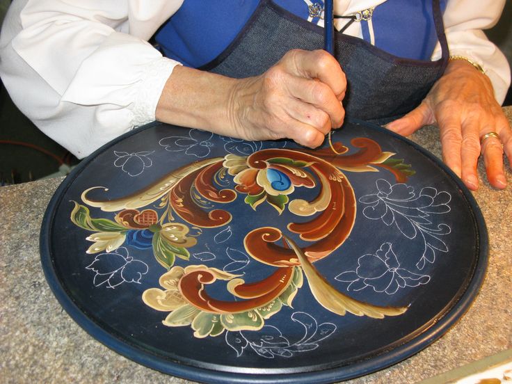 a man in an apron is working on a decorative plate with flowers and leaves painted on it