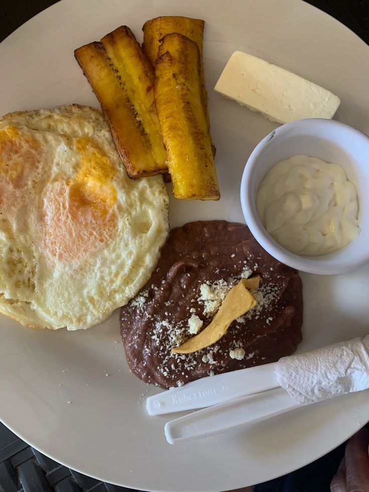 a white plate topped with eggs, bread and other foods next to a cup of sauce