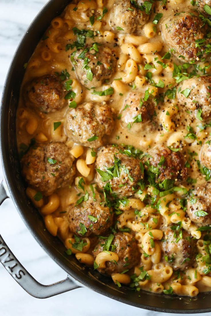 a pot filled with pasta and meatballs on top of a white marble countertop