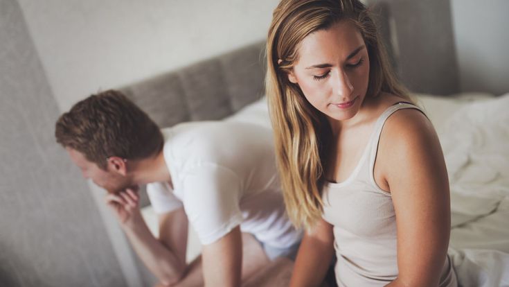 a man and woman sitting on a bed looking at each other's stomachs