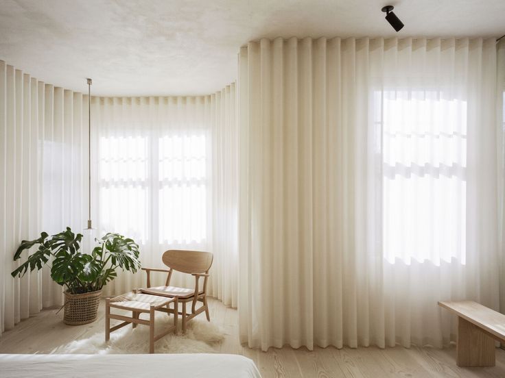 a bedroom with white curtains and a chair