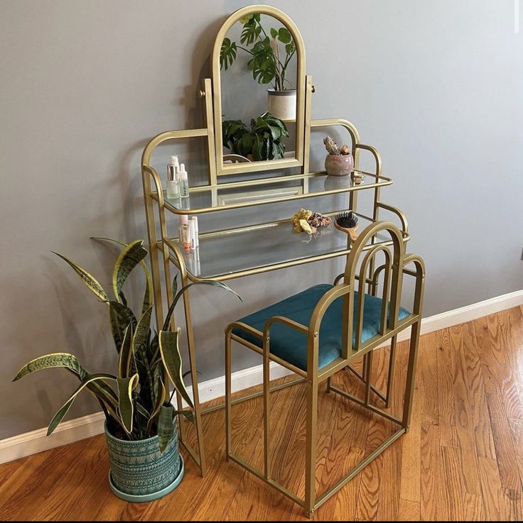 a gold vanity with mirror and stool next to a potted plant on the floor