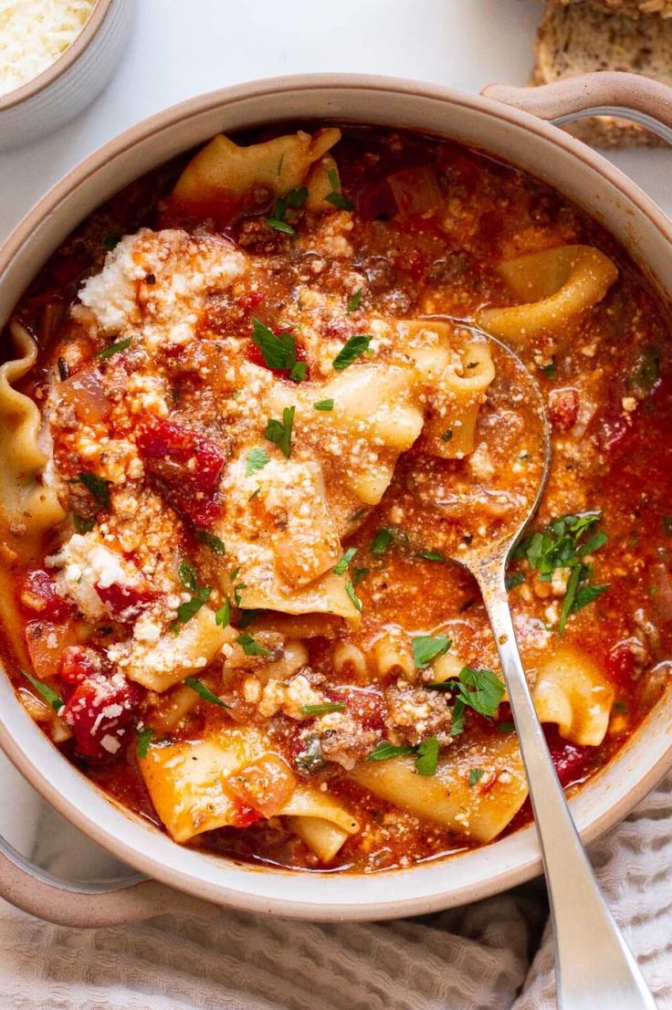 a white bowl filled with pasta and sauce on top of a table next to bread