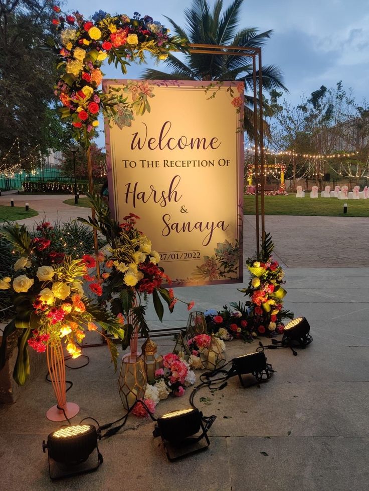 a welcome sign with flowers and candles on the ground in front of some palm trees