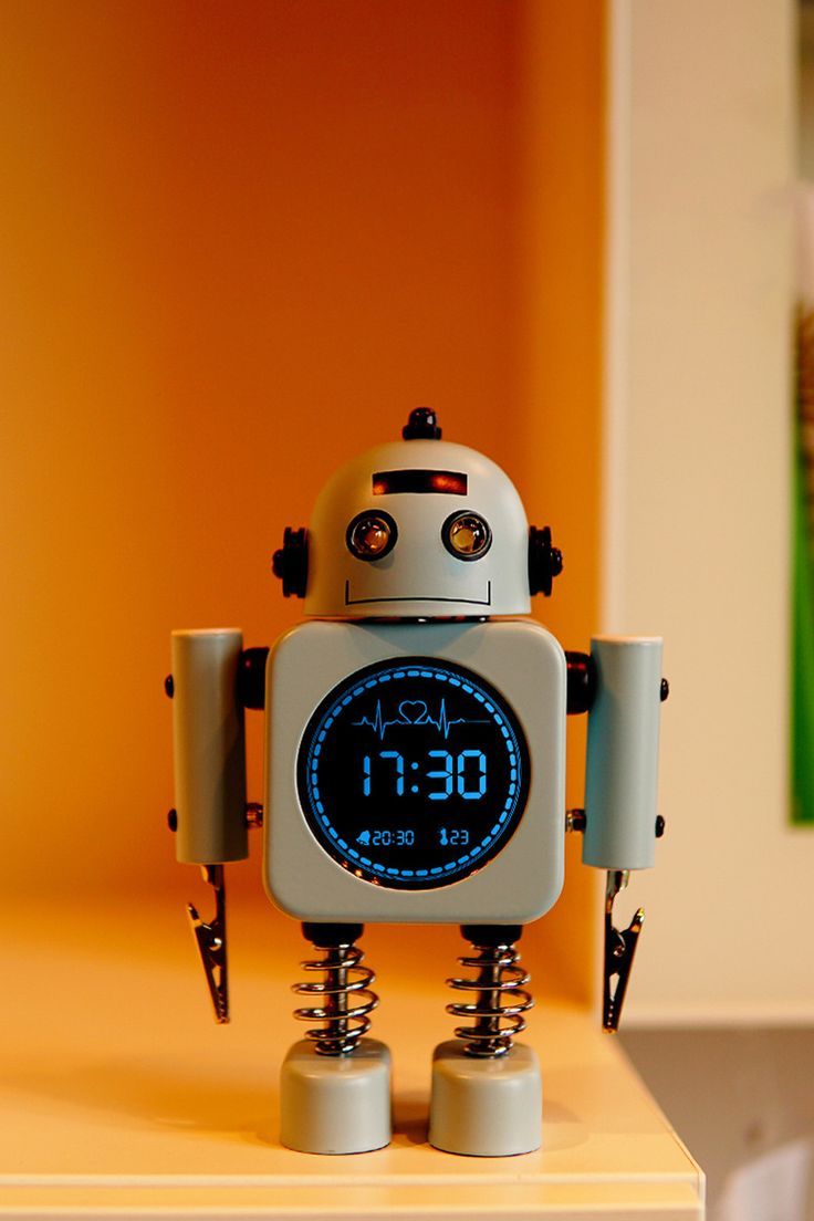 a robot that is sitting on top of a table with an alarm clock in front of it