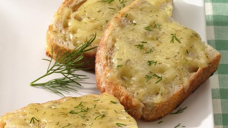 two pieces of bread with cheese and dill on them sitting on a white plate