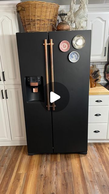 a black refrigerator in a white kitchen with wood flooring and lots of cupboards