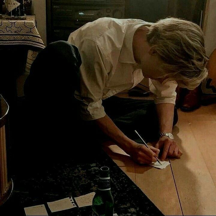 a man writing on a piece of paper in front of a fire place with candles