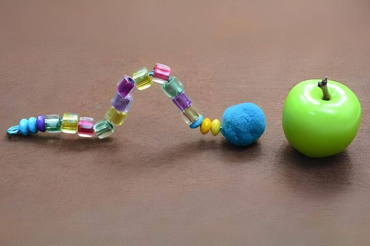 an apple, bead necklace and green apple on a brown surface with one beaded apple in the foreground