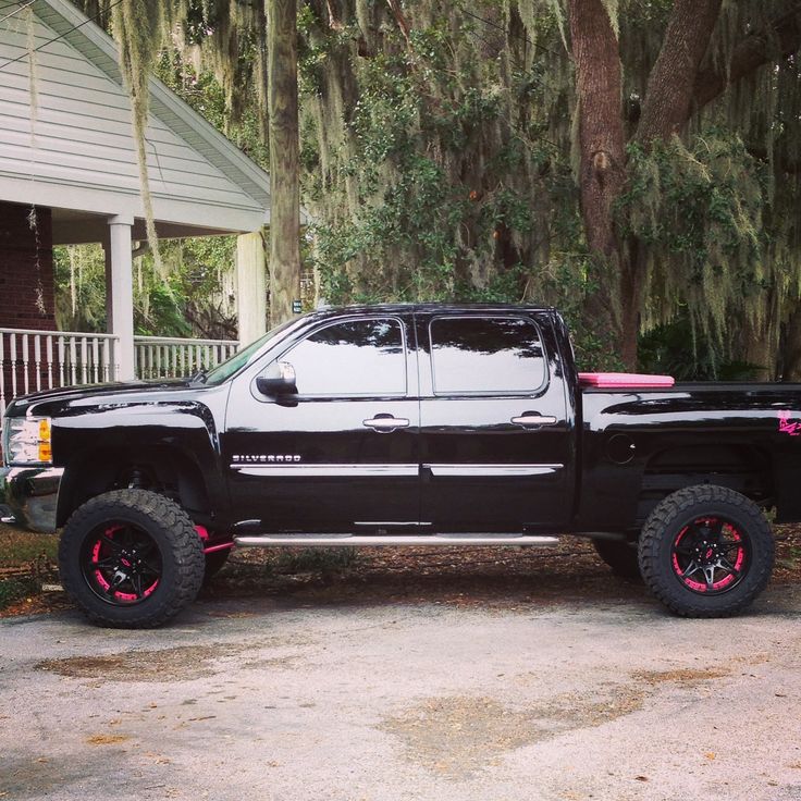 a black truck with pink rims parked in front of a house on a driveway