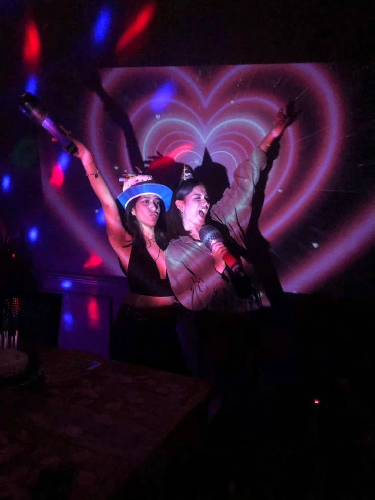 two people are dancing in the dark with their arms up and one person is wearing a hat