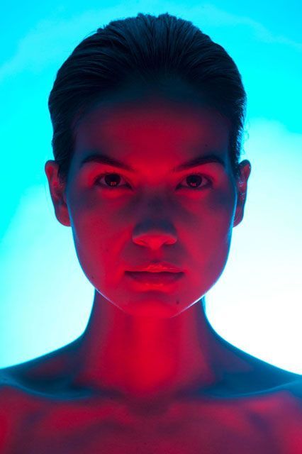 a woman with red light on her face and chest in front of a blue background