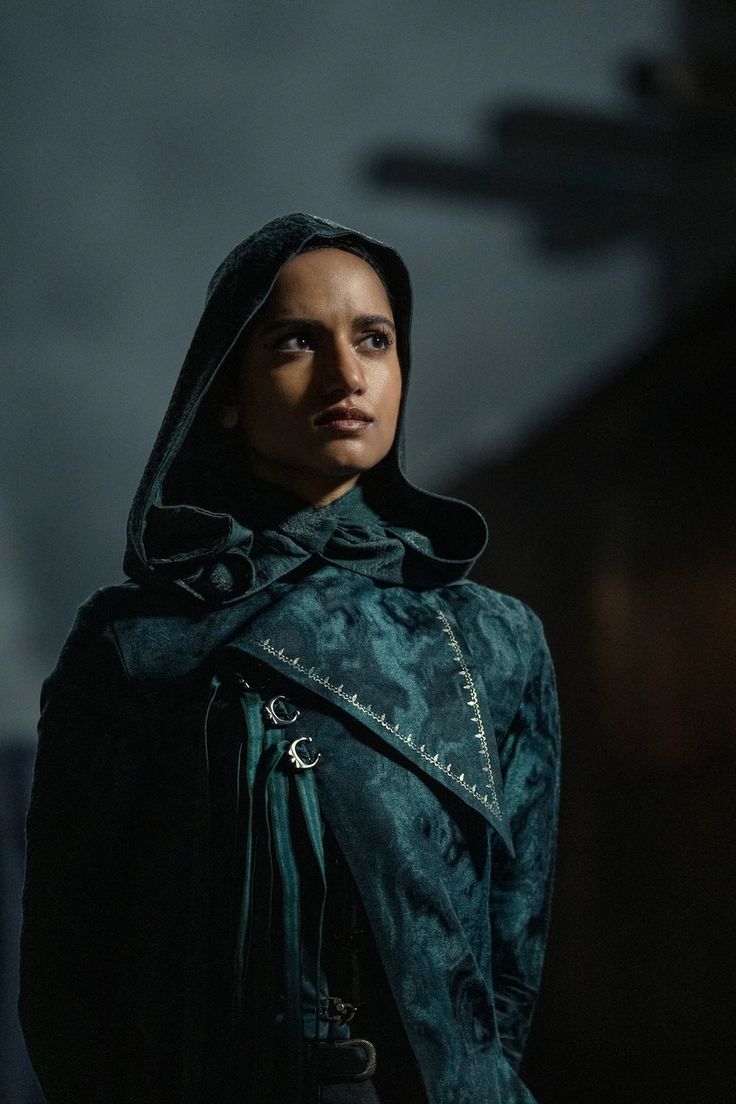 a woman with a hoodie on standing in front of a dark background and looking at the camera