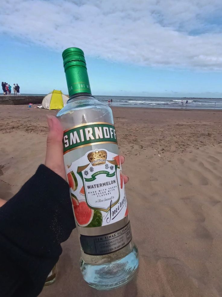 someone holding up a bottle of water on the beach