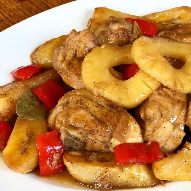 a white plate topped with chicken and pineapples covered in sauce on top of a wooden table