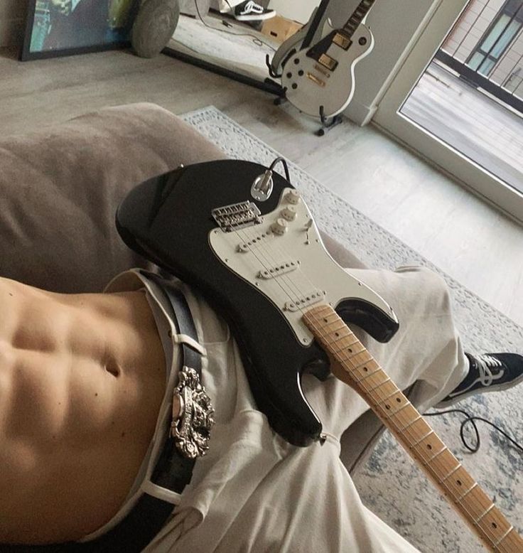 a man laying on top of a couch with a guitar strapped to his chest next to him