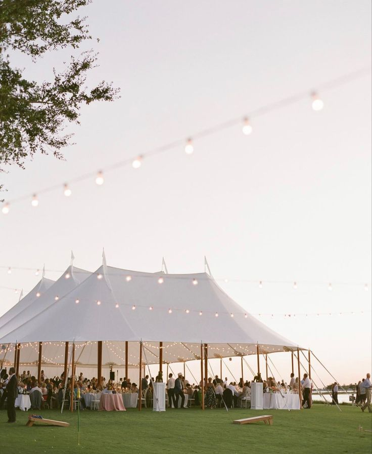 a large white tent is set up with string lights and people sitting at the tables