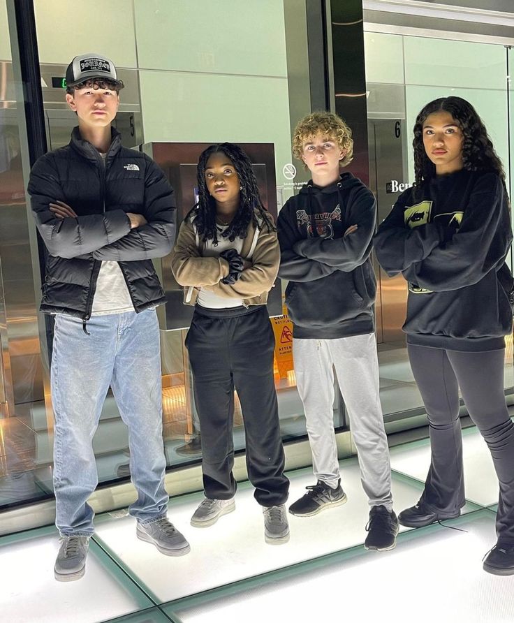 four young men and women standing in front of a glass wall with their arms crossed