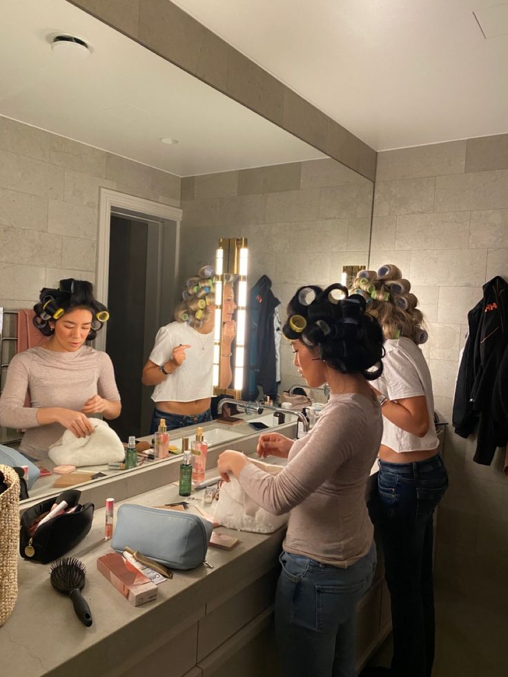 two women are doing their hair in front of the mirror while another woman is drying her hair