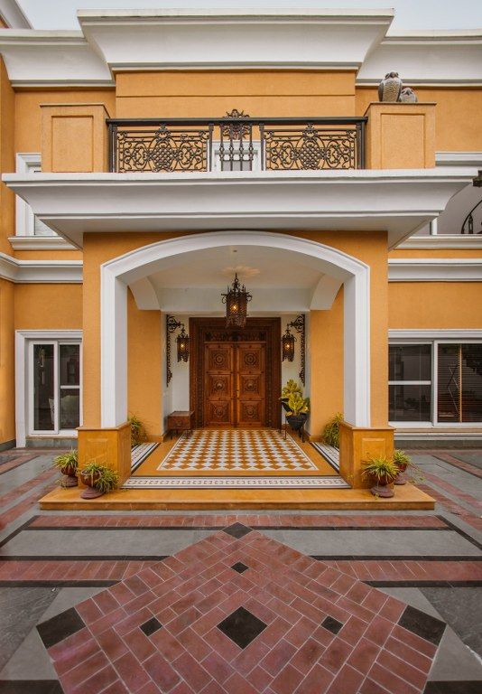 the entrance to a large yellow house with white trim and columns on either side, surrounded by brick pavers