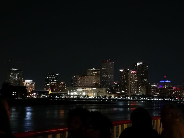 the city skyline is lit up at night as people sit on benches near the water