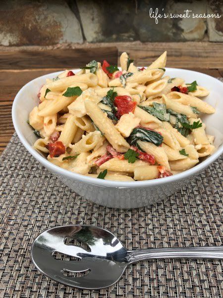 a white bowl filled with pasta and spinach on top of a table next to a spoon