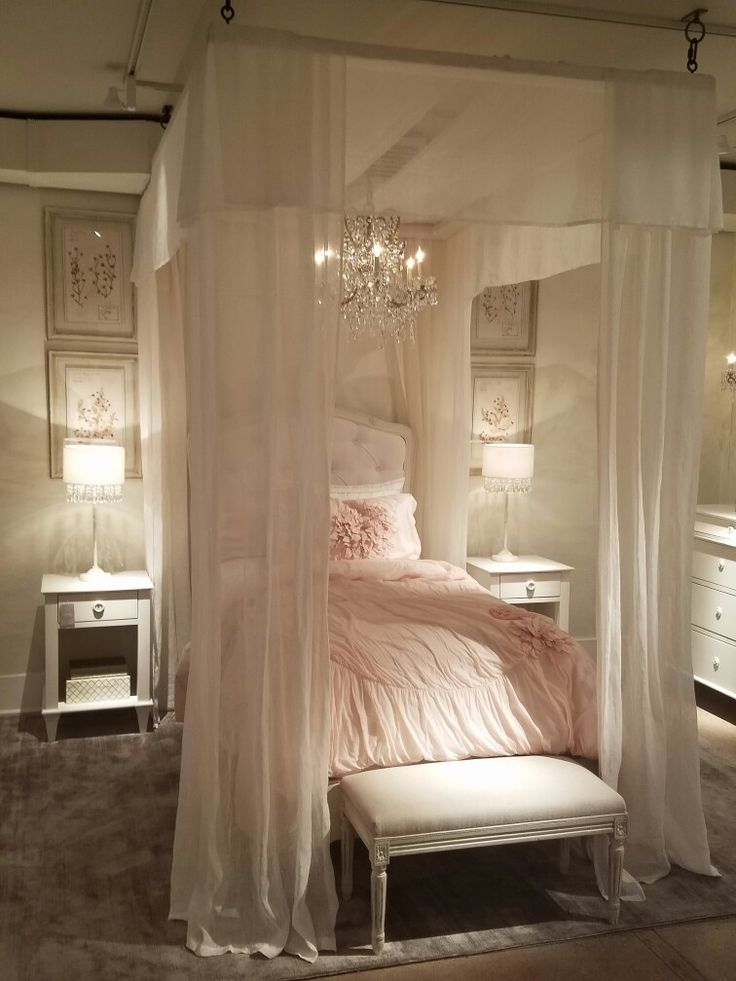 a white canopy bed in a bedroom with chandelier and pillows on the floor