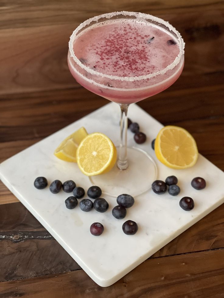 a drink sitting on top of a white plate next to blueberries and lemons