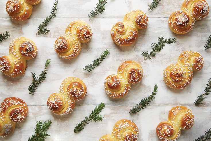 several pastries are arranged on a white surface with green sprigs and pine needles