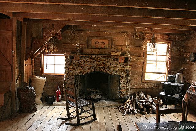 an old fashioned living room with rocking chair and fireplace in the center, surrounded by wood flooring