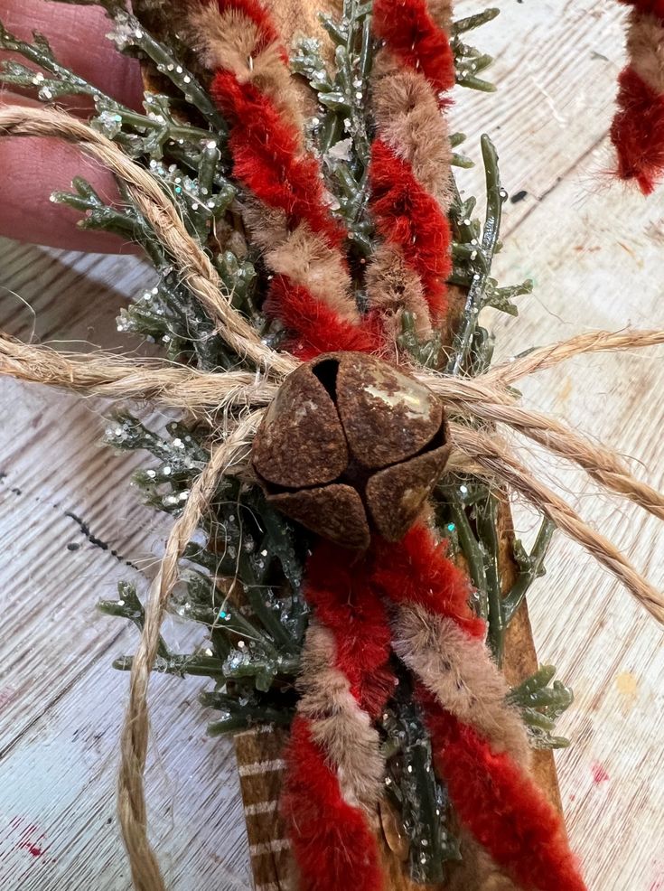 a hand holding a piece of wood with some red and white decorations on top of it