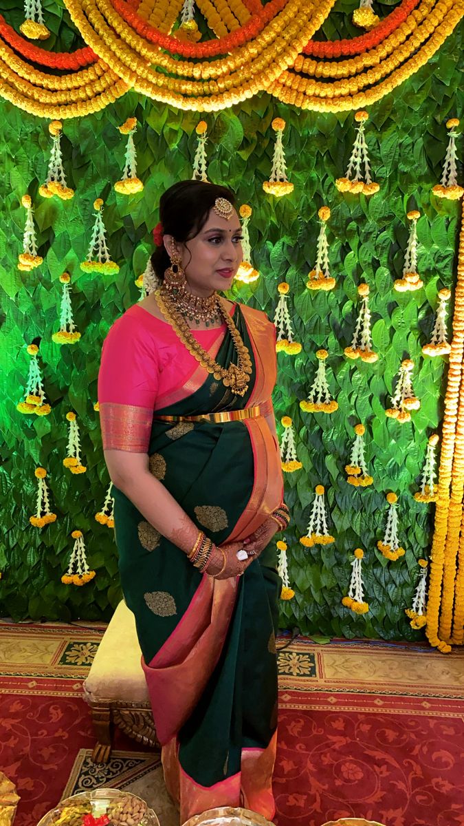 a woman in a green and pink sari standing next to a wall with gold decorations