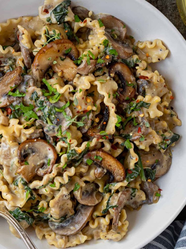 pasta with mushrooms, spinach and cheese in a white bowl on top of a table